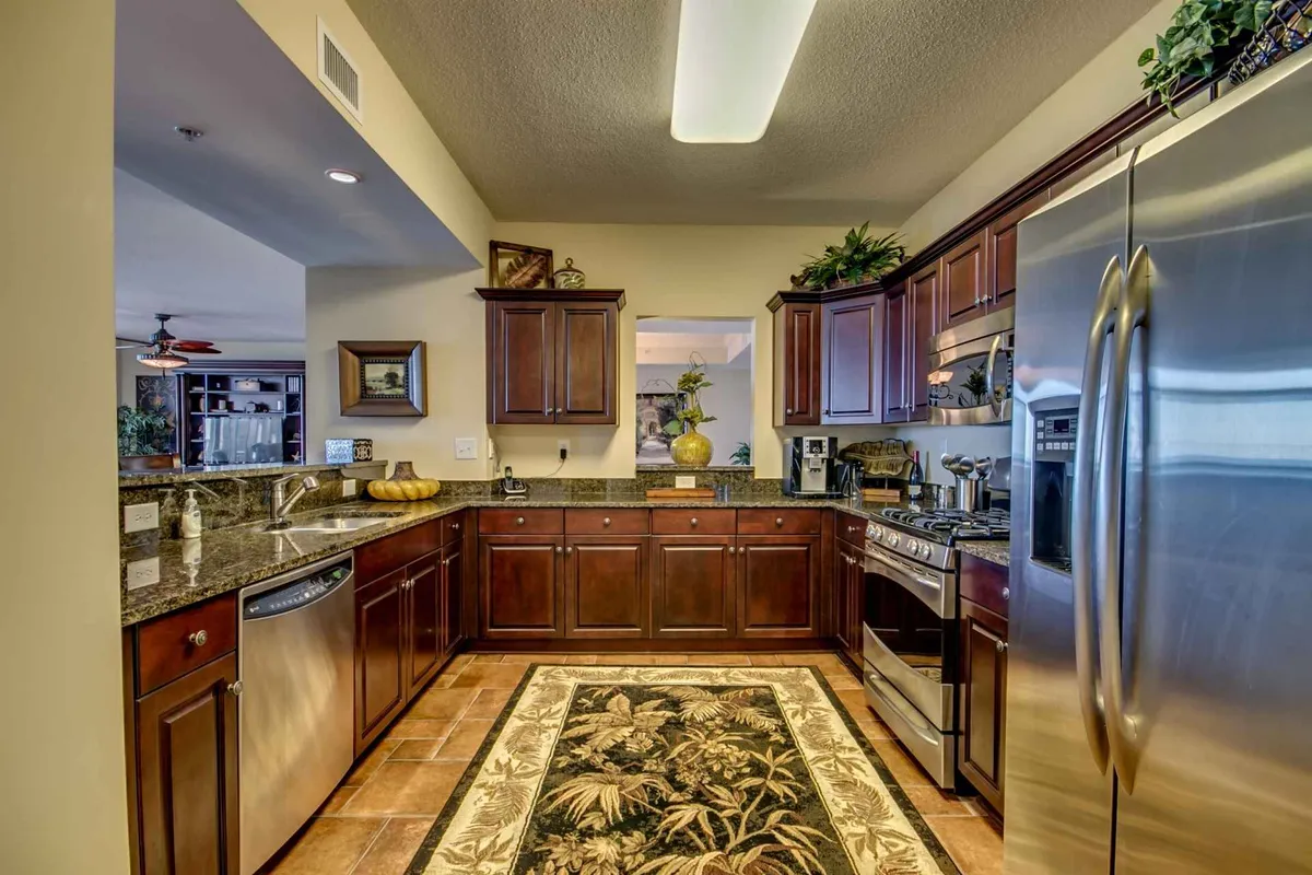 This image highlights a modern kitchen with gleaming stainless steel appliances, granite countertops, and a decorative plant, all set atop an area rug. The layout is open and inviting, suggesting space for both meal preparation and group gatherings.