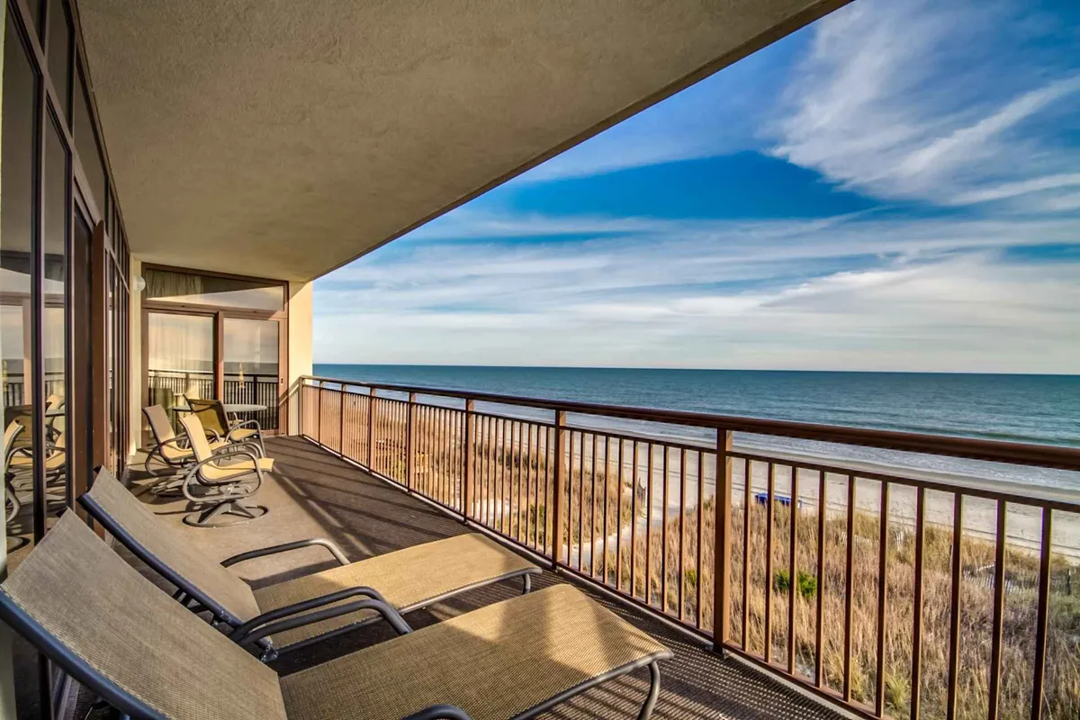 This image showcases a spacious condo balcony overlooking the ocean, with inviting seating perfectly situated for taking in sweeping water views. The sky stretches across the horizon, creating a tranquil backdrop, and the setup suggests opportunities for relaxing, reading, or enjoying the fresh sea breeze at sunrise or under the stars.