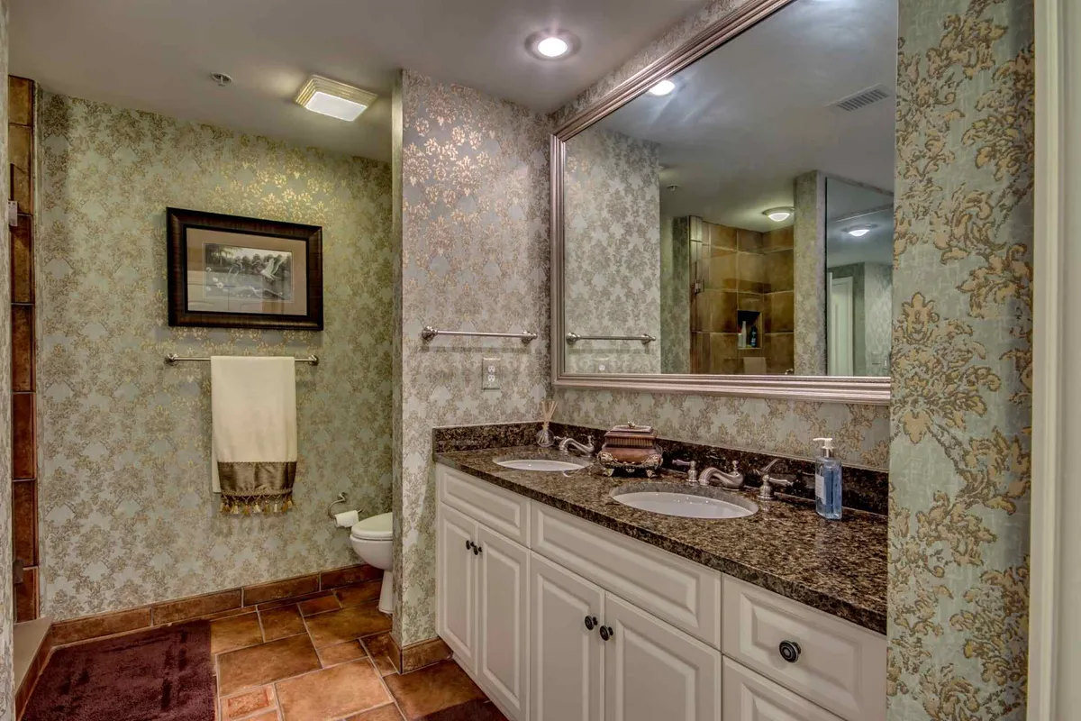 A sophisticated bathroom with a double vanity, elegant framed artwork, and an ornate wall design. The space is well-lit and inviting, ideal for relaxation and morning routines.