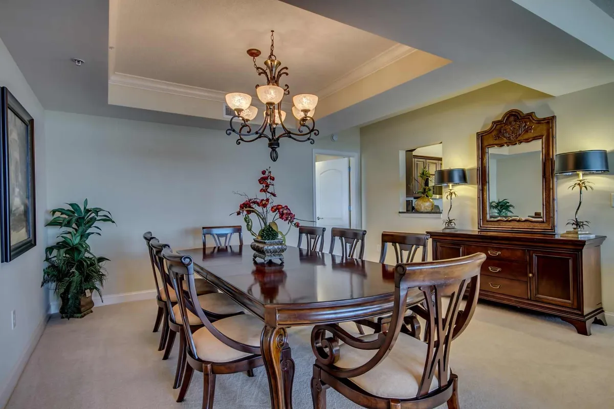 An elegant dining area featuring a wooden table set beneath a sparkling chandelier, complemented by a floral centerpiece and softly glowing lamps. The space is warm and welcoming—ideal for family-style meals, celebrations, or intimate dinners with friends.