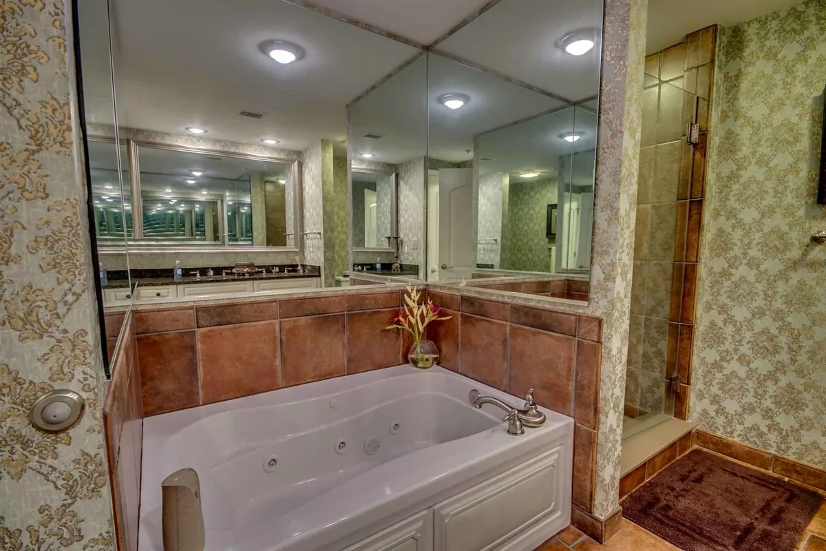 A serene interior space featuring an opulent jacuzzi tub, large mirrors, and tasteful decorative wall patterns. The setting conveys a spa-like atmosphere, perfect for relaxation and self-care.