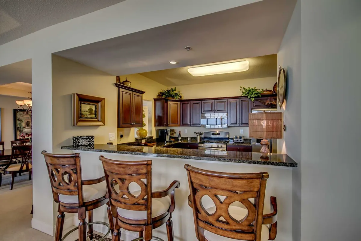 The photo features a stylish bar counter adjacent to kitchen cabinets, with decorative items adding a touch of warmth. The scene is set up for both cooking and socializing, suggesting a casual spot for coffee or wine with friends.